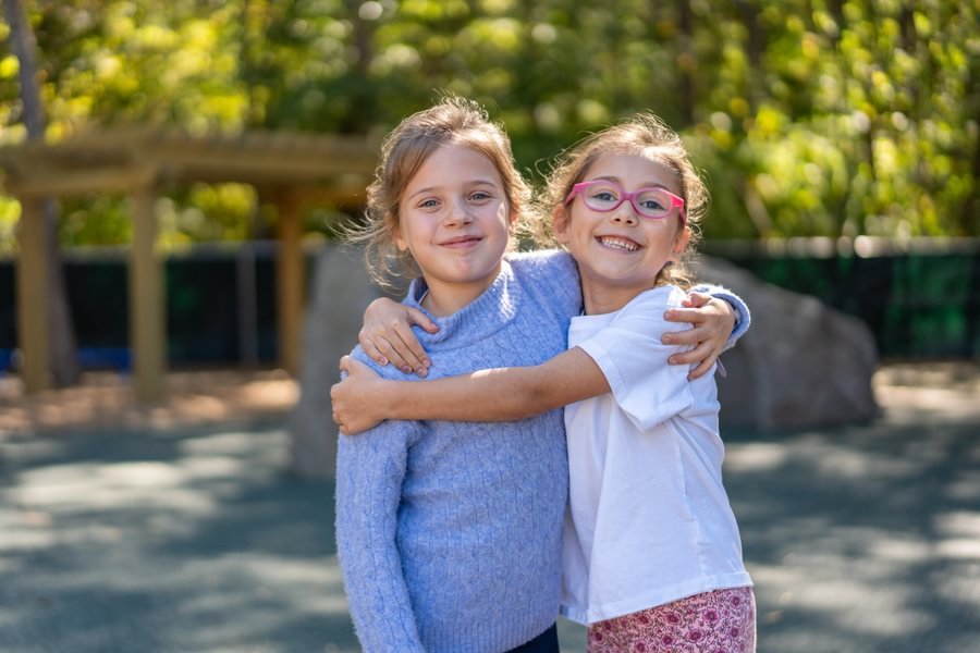 Two students hugging and smiling on playground.