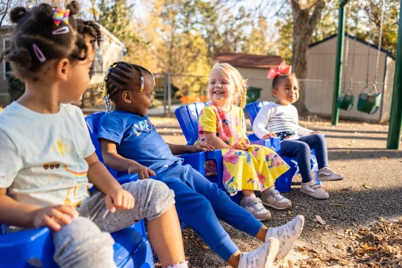 Four students laugh together outside on chairs.