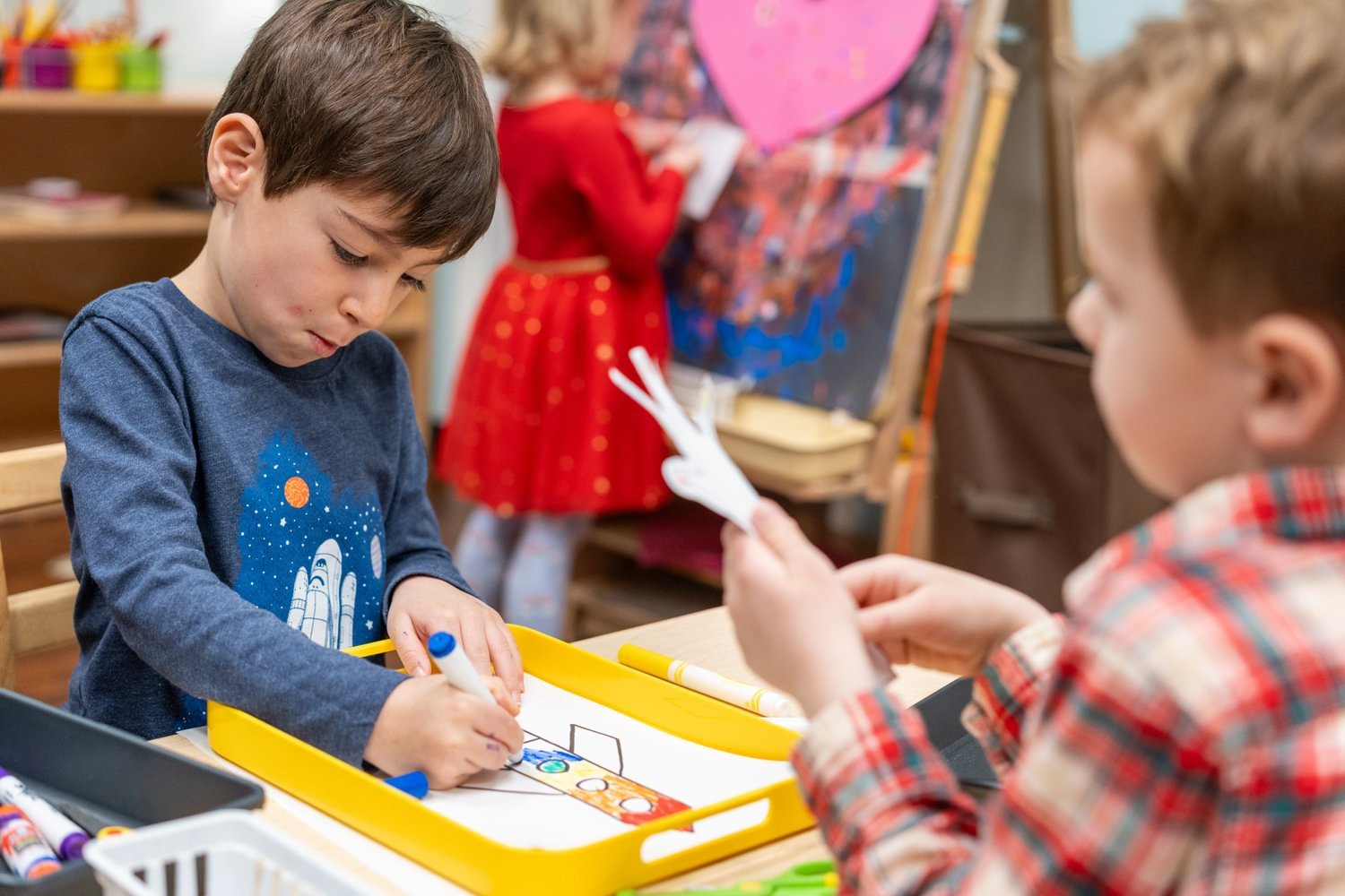 Two boys work on projects with art supplies.