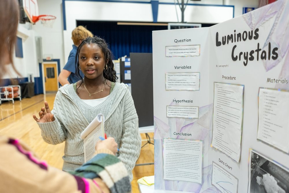 A girl explains her project next to a descriptive trifold.