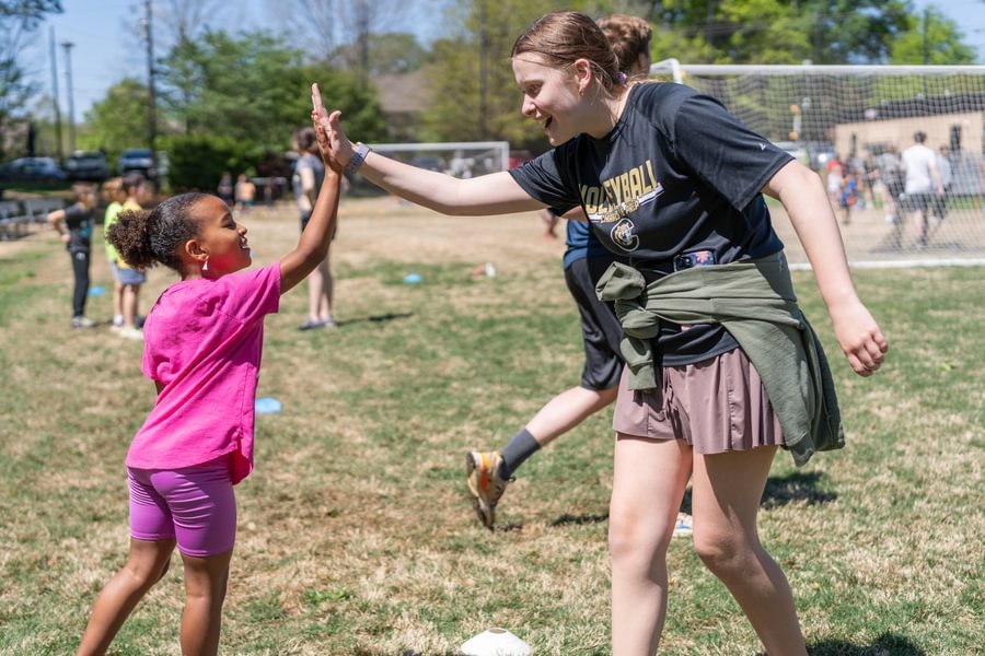 An older boy helps a smiling younger student with a project.