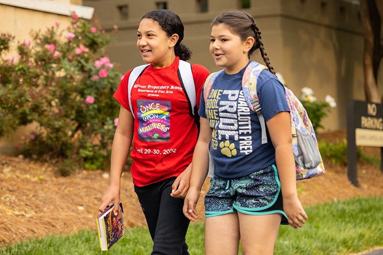 Two older girls walk next to each other carrying books and smiling