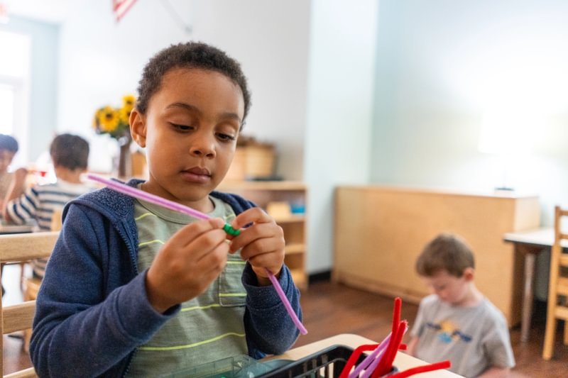A focused student puts beads on a straw.