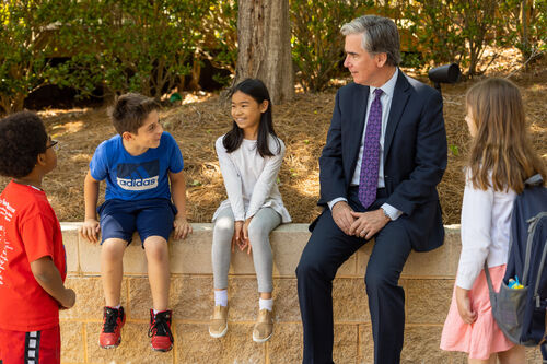 Head of School Chris Marblo sits with children on a wall