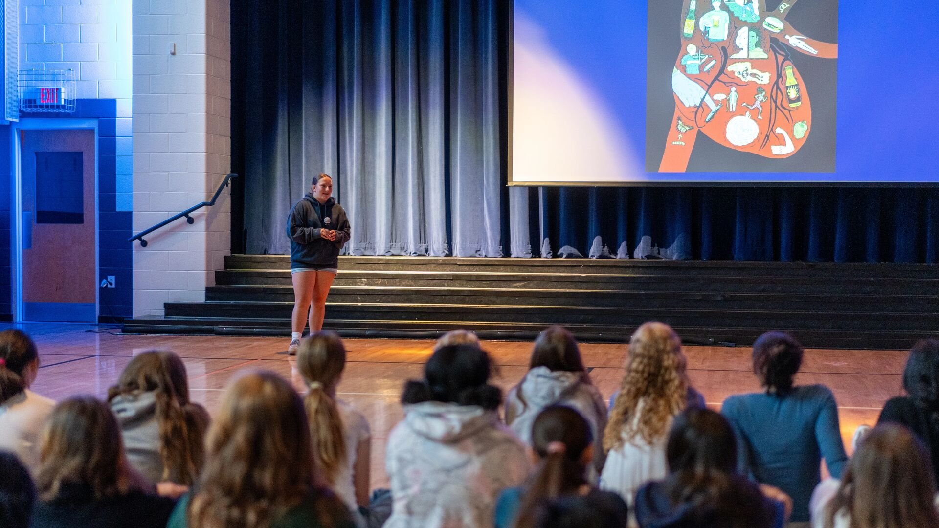 Student on stage in a spotlight with a slideshow