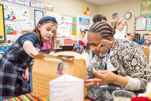 A student points out details of her lunch box to a guest